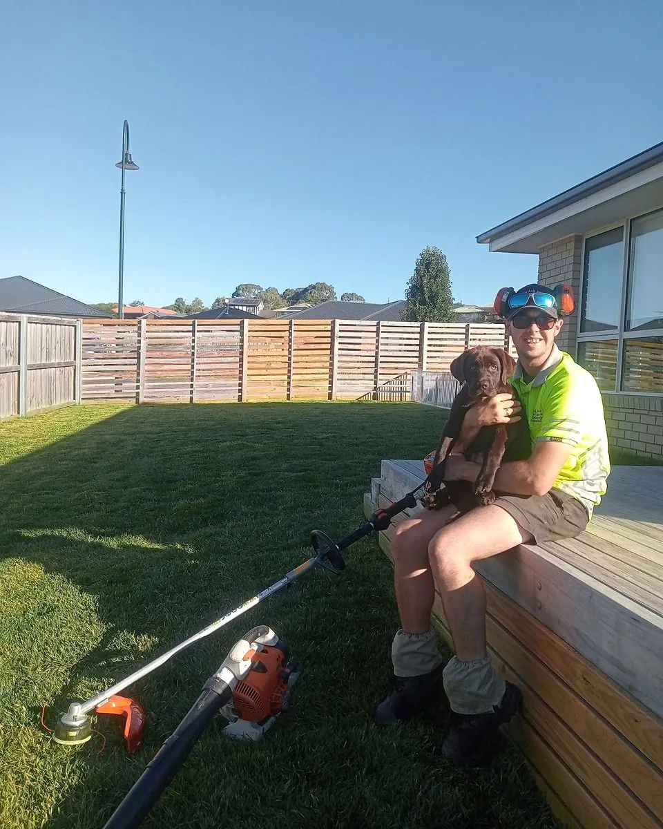 Josh Bitz sitting beside a finished lawn with a young dog